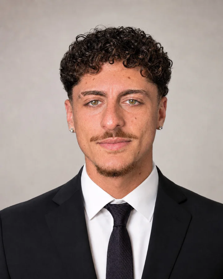 Portrait of Estivan Ayramia wearing a dark suit, white shirt, and tie